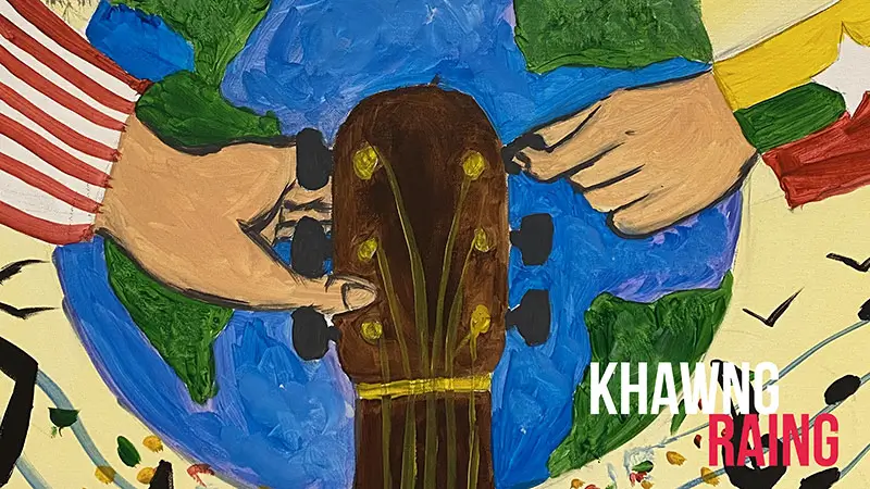 Scholarship winner Khawng Raing, beside a painting of hands holding a guitar over a globe.