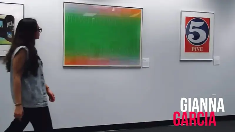 Scholarship winner Gianna Garcia walking past framed artwork in a gallery.