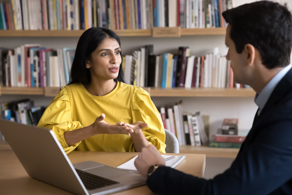 Female student having a discussion with her male advisor in a library.