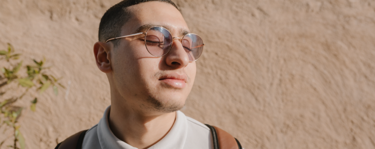 Joven con gafas de sol, de aspecto relajado, frente a un fondo de estuco.